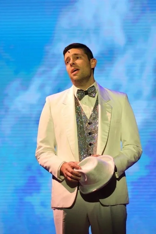 Michael Mingoia performing on stage in a white tuxedo, bringing 20 years of professional stage experience to M3 Studios in Patchogue, NY